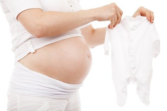 A pregnant woman holding baby’s sleepers