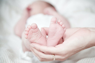 A hand holding tiny baby’s feet while it sleeps.