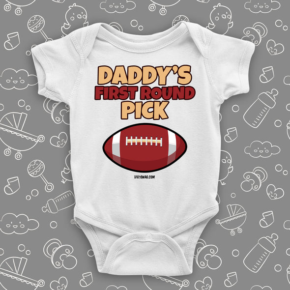 Cool baby onesie saying "Daddy's first round pick" and including the image of a football, color white.