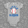 Graphic baby onesies with baseball print on it and saying "Little Slugger" in grey 